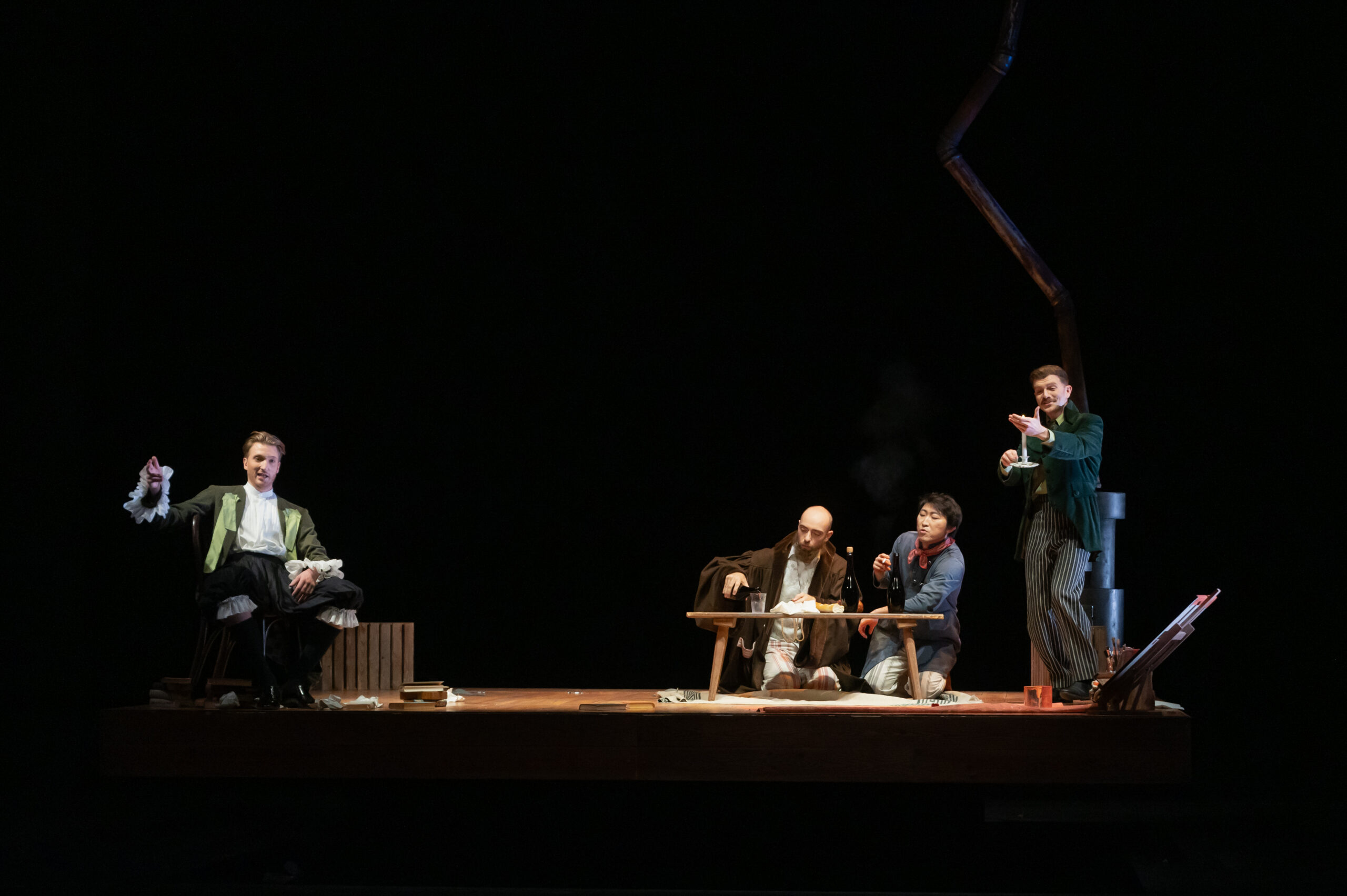 Bühnenbild und Kostüm von Lisa Behensky für La Bohème – Gruppe von Figuren an Tisch auf leerer Bühne mit reduzierter Raumstruktur