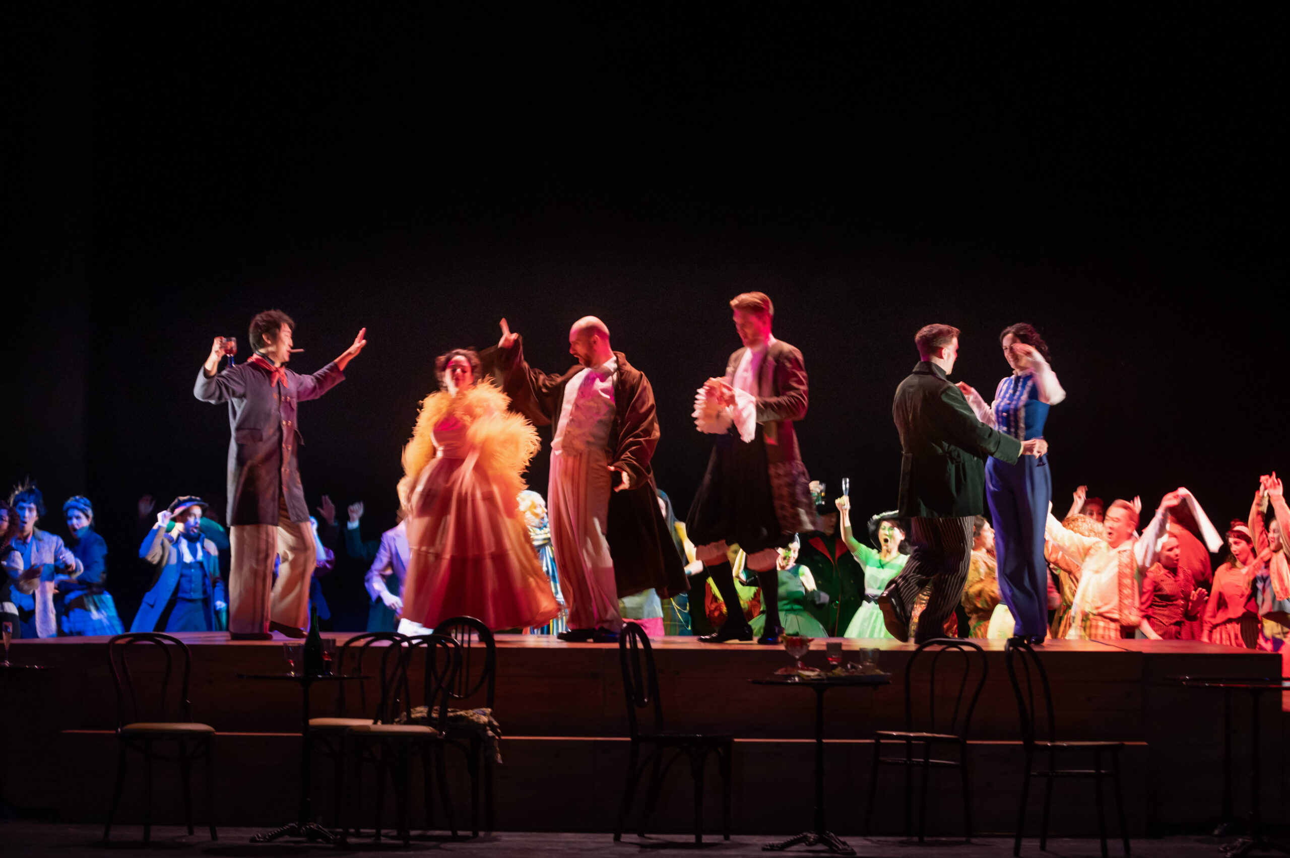 Szenografie und Kostüm von Lisa Behensky für La Bohème – Ensemble in farbigen Kostümen auf erhöhter Bühne mit Tanzszene