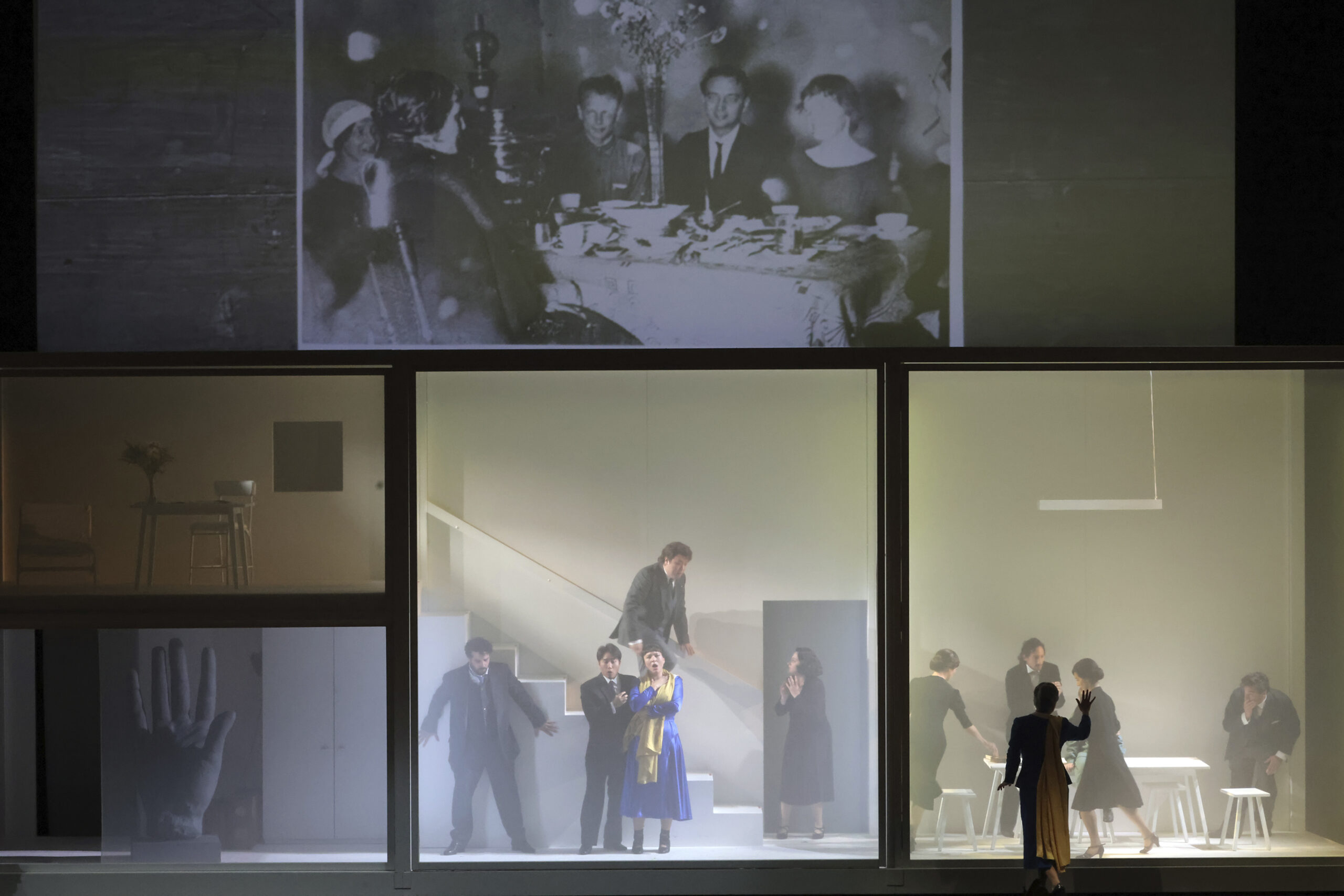 Szenografie von Lisa Behensky für Anna A. – fragmentierter Bühnenraum mit Treppe, mehreren Figuren und historischer Projektion