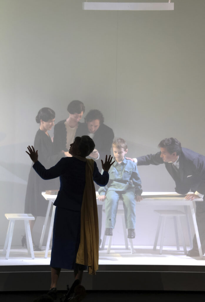 Szenografie von Lisa Behensky für Anna A. – fragmentierter Bühnenraum mit Treppe, mehreren Figuren und weichem Lichteinfall hinter Tüll 