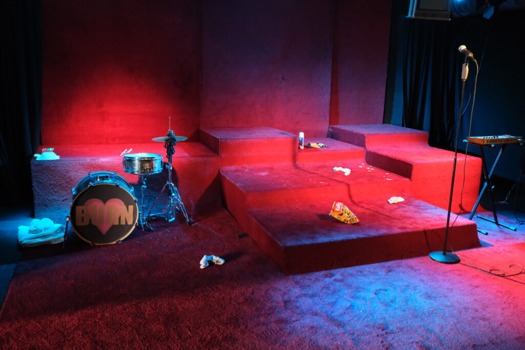 Szenografie und Kostüm von Lisa Behensky für Phaidras Liebe rotes Teppich Bühnenbild  mit Musikinstrumenten und starkem Lichtakzenten